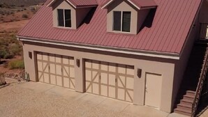 Una casa de dos pisos con techo rojo, un garaje con dos puertas y una escalera que sube al segundo piso.