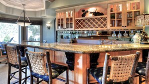 Zona de bar con mostrador de madera, taburetes y una estantería para vinos.