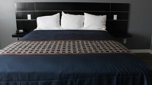 A neatly made bed with a patterned bedspread and pillows, a black headboard, and a bedside table with a phone and a small item on it.