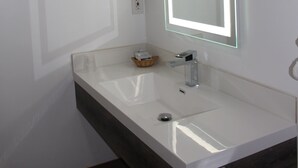 A modern bathroom with a white sink, a mirror with LED lighting, and a dark-toned vanity.