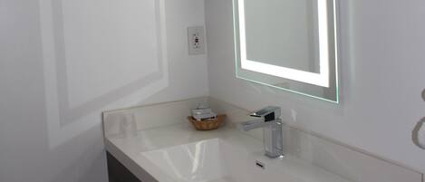A modern bathroom with a white sink, a mirror with LED lighting, and a dark-toned vanity.