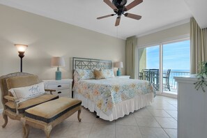 Une chambre à coucher comprenant un lit, une chaise, une table de chevet, une lampe, un ventilateur de plafond et un balcon avec vue sur l’océan.