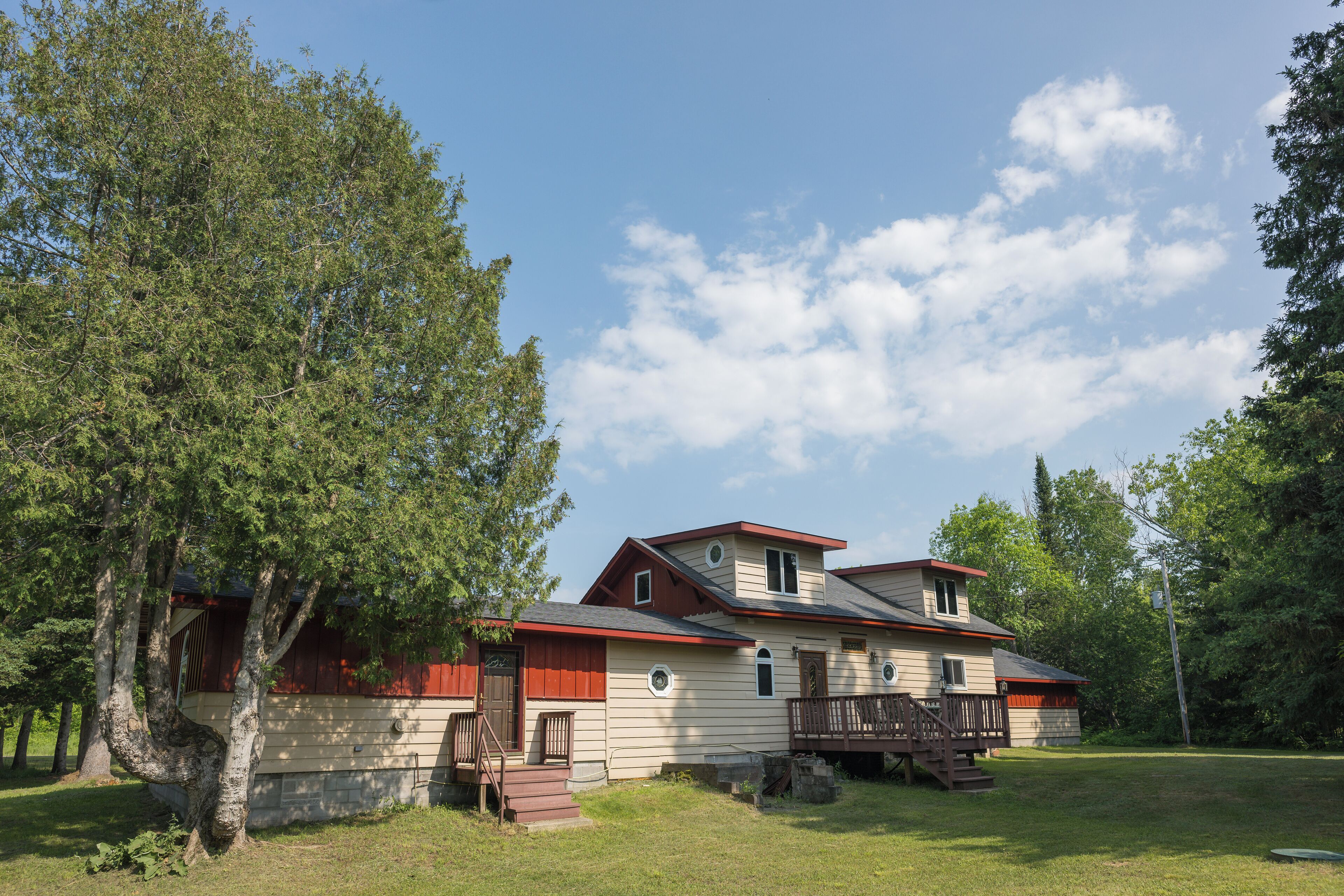 A two-story house with a red roof, a front porch, and a small deck.