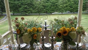 Uma mesa posta para refeição, com centros de mesa florais, talheres e copos.