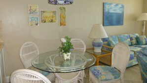 A dining area with a glass table surrounded by wicker chairs, a white lamp, and a blue sofa. - Seawinds  Beautiful Beachfront Renovated Condo. Watch the dolphins go by! (Marco Island)
