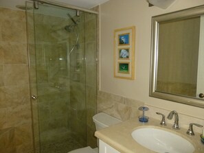 A bathroom with a glass-enclosed shower, a sink with a mirror above it, and three framed pictures on the wall. - Seawinds Beautiful Beachfront Renovated Condo. Watch the dolphins go by! (Marco Island)