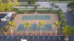 An aerial view of a parking lot with two tennis courts, surrounded by palm trees and a flagpole. - Seawinds  Beautiful Beachfront Renovated Condo. Watch the dolphins go by! (Marco Island)