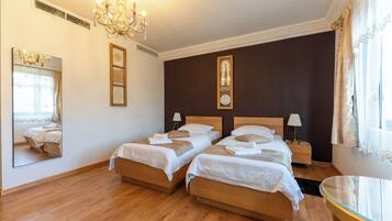A hotel room with two wooden beds, a chandelier, a mirror, and a bedside table with a lamp.
