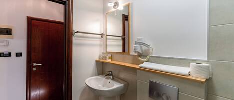 A bathroom with a wooden door, a white sink, a mirror with lights, a towel rack, and a toilet.