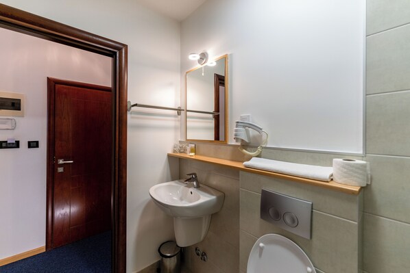 A bathroom with a wooden door, a white sink, a mirror with lights, a towel rack, and a toilet.