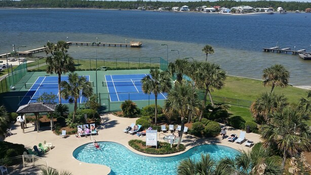 Een resort met een zwembad, tennisbanen en uitzicht op het water.