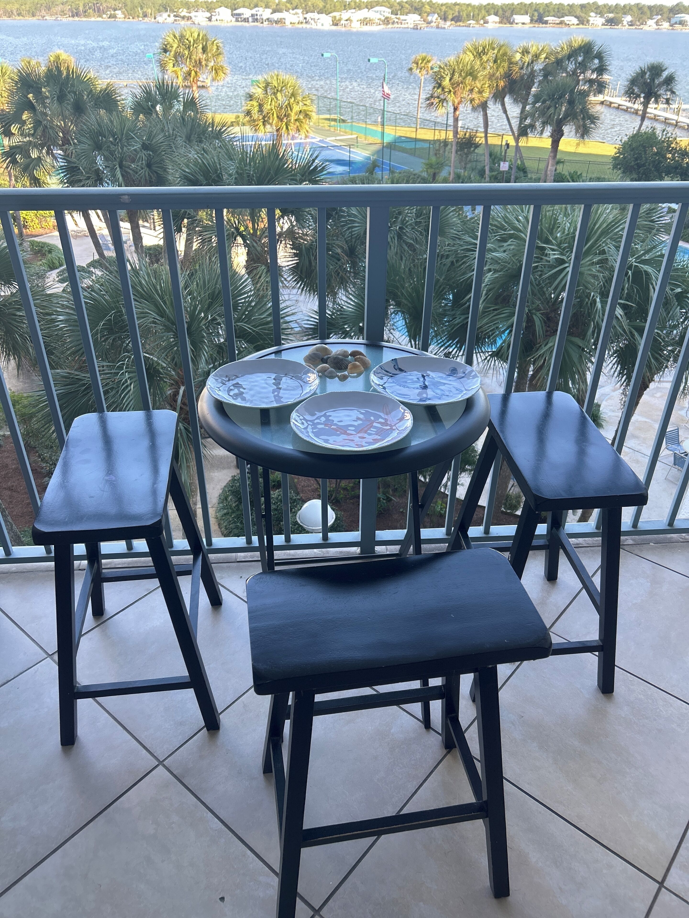 Un balcon avec une table ronde et quatre chaises, donnant sur une étendue d’eau et des palmiers.
