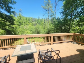 A wooden deck with a table and chairs, surrounded by a wooden railing, overlooking a forested area.