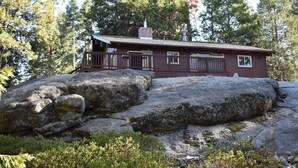En stuga med en veranda, omgiven av stora stenar och tät skog.