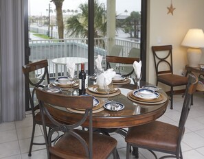 A round dining table with six chairs, set with plates, glasses, and a bottle of wine.