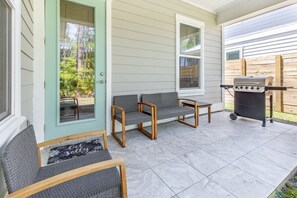 Eine Terrasse mit zwei grau gepolsterten Stühlen, einem kleinen Tisch und einem Grill.