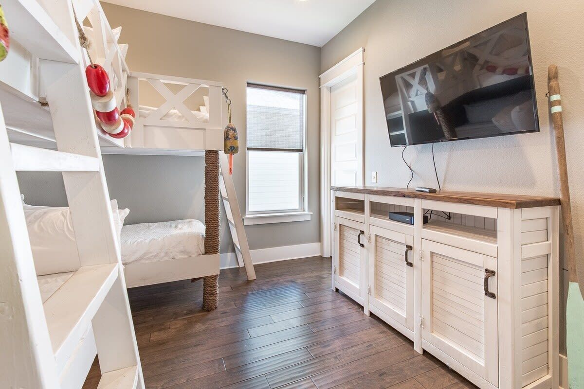 A bunk bed with a ladder, a television mounted on the wall, and a window with blinds.