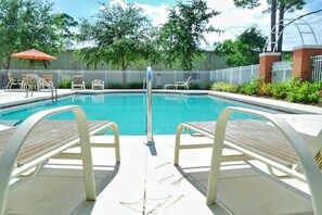 A swimming pool with a metal ladder, surrounded by white chairs and a white fence.