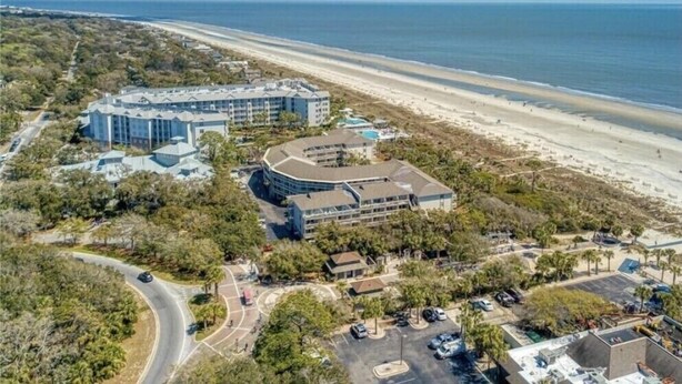 Vista aérea de um hotel à beira-mar com vários edifícios, uma praia e estacionamento.