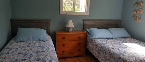 A bedroom with two beds, a nightstand with a lamp, and a window with blinds.