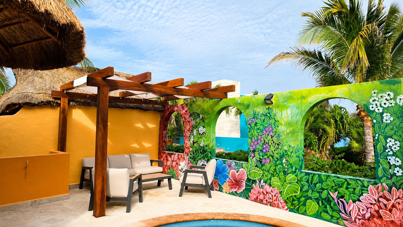 A poolside area with a wooden pergola, outdoor seating, and a colorful mural.