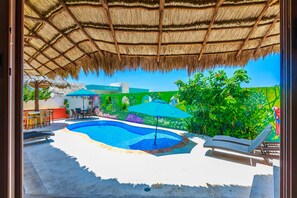 A swimming pool with a thatched roof, lounge chairs, and umbrellas. - Charming Private Retreat sleeps 6 with ocean views! (Isla Mujeres)