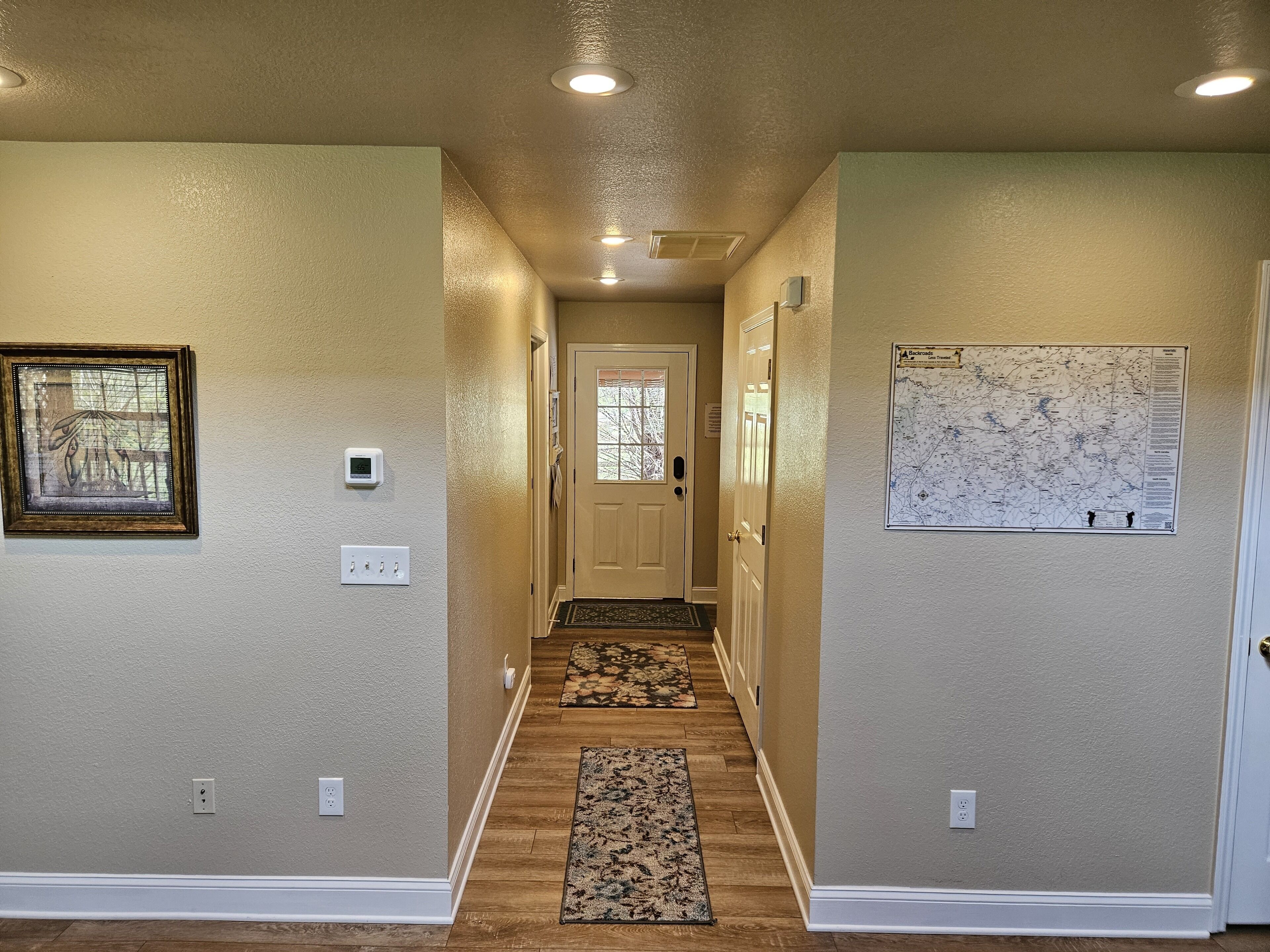A hallway with beige walls, a framed picture, a map, and a door at the end.