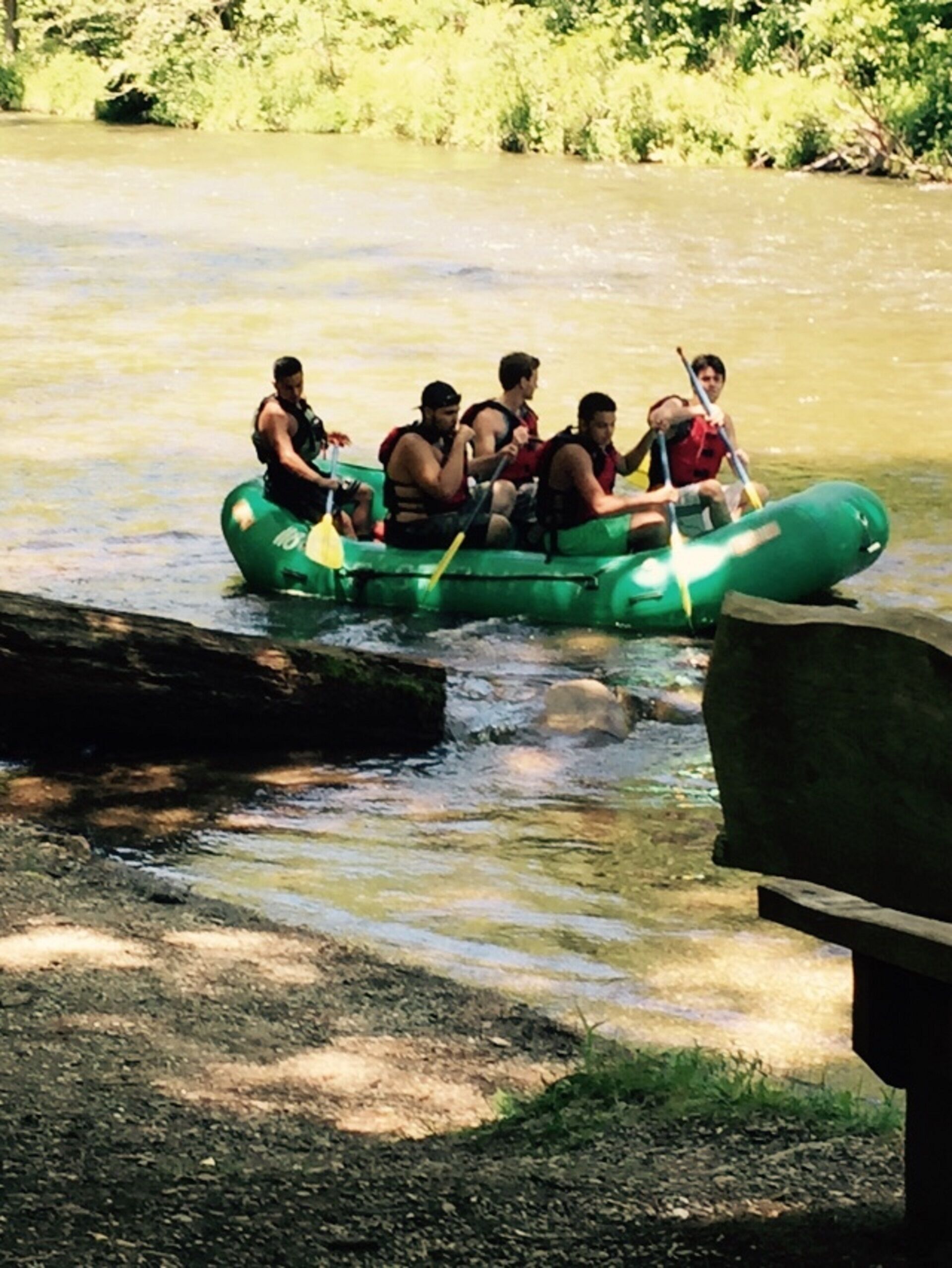 A group of people in a green raft on a river.