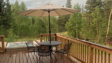 A wooden deck with a hot tub, two chairs, and a table under a large umbrella.