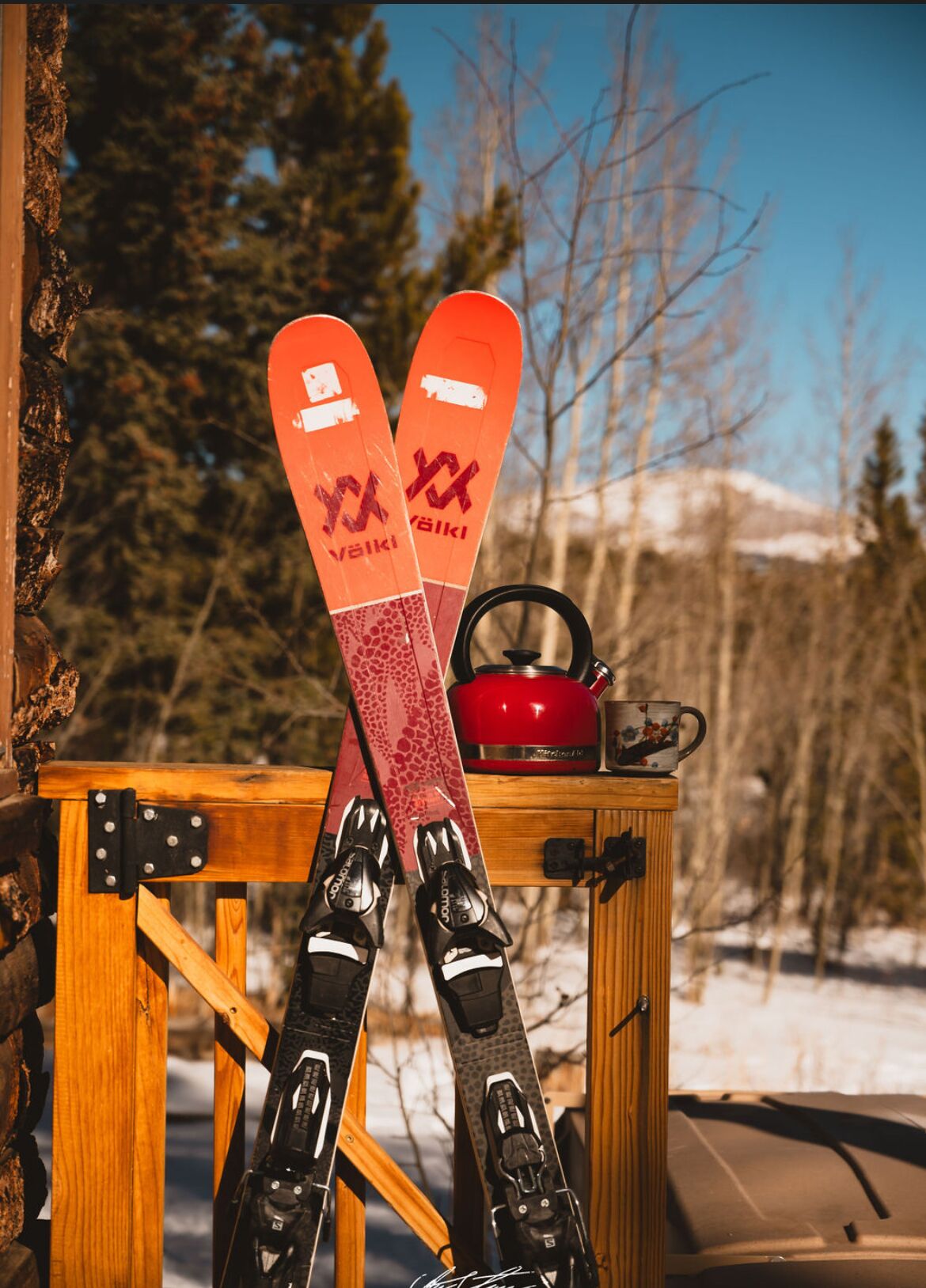 A pair of skis leaning against a wooden structure with a red kettle and a mug on top.