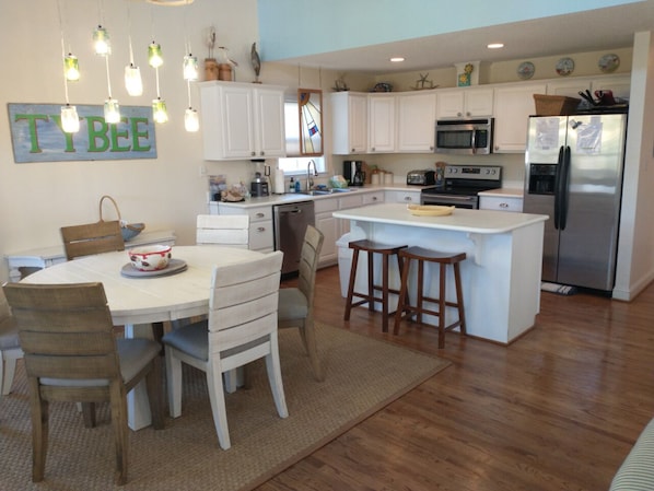 A modern kitchen with white cabinets, a central island, and a dining area with wooden chairs.