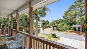 A wooden porch with a bench and a table, overlooking a street with houses and trees. - Peaceful House on South Island with Bikes- discounts on weekly summer stays! (Tybee Island)
