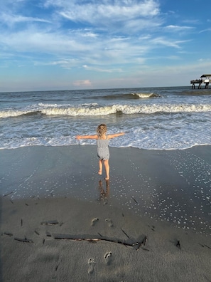 A child standing on a sandy beach with waves in the background.