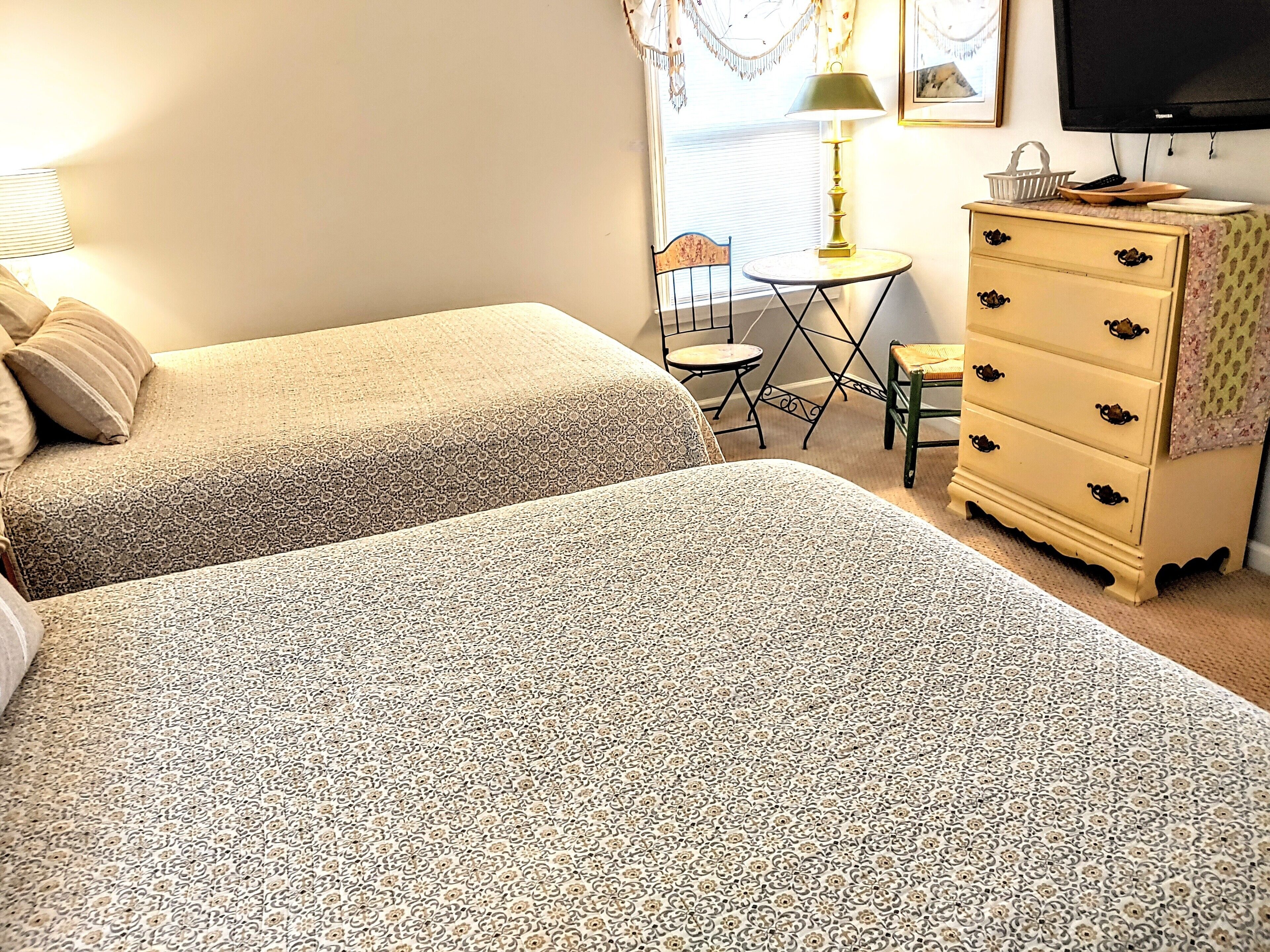 Une chambre avec deux lits, une commode, une chaise, une table et un téléviseur.