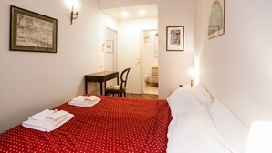 Een hotelkamer met een bed, een bureau en een stoel. Twee ingekaderde foto's hangen aan de muur.