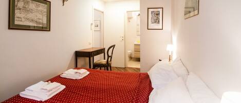 Ein Hotelzimmer mit einem Bett, einem Schreibtisch und einem Stuhl. An den Wänden hängen zwei gerahmte Bilder.