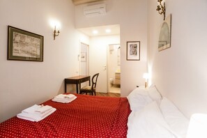 Ett hotellrum med en säng, ett skrivbord och en stol. Det finns två inramade tavlor på väggarna.