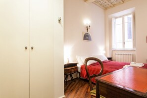 A bedroom with a wooden bed, a desk, a chair, a radiator, and a window with shutters.