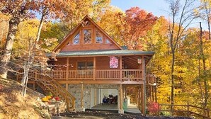 A wooden cabin with a balcony, surrounded by autumn foliage. - Quiet Cabin Nestled in trees with King -hot tub, pool, pool table, fishing pond (Sevierville)