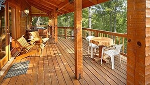 A wooden deck with outdoor seating, including chairs and a table, and a clock on the wall. - Quiet Cabin Nestled in trees with King -hot tub, pool, pool table, fishing pond (Sevierville)
