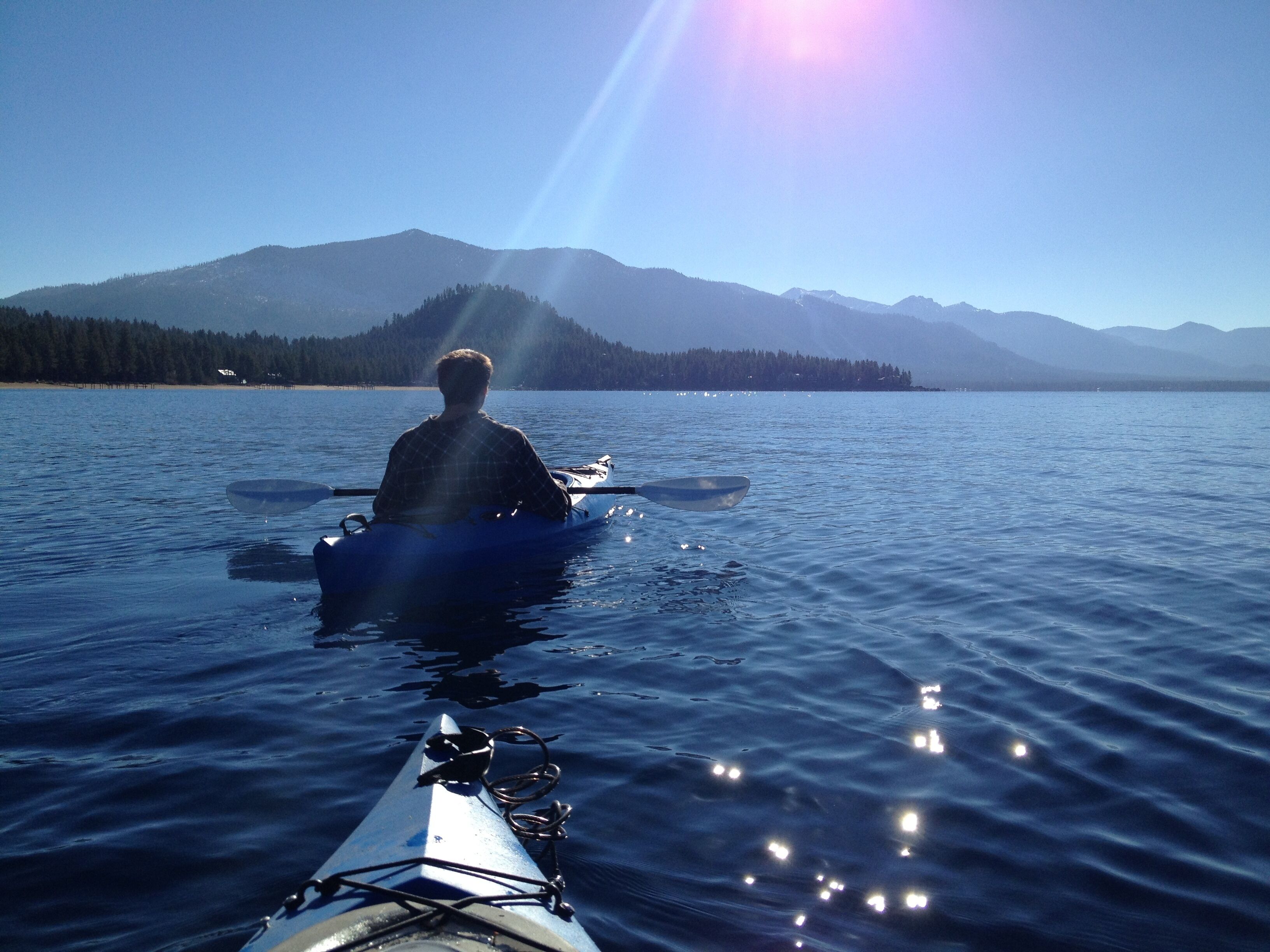 A person in a kayak on a calm lake with mountains in the background.