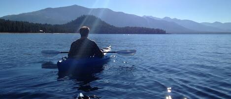 A person in a kayak on a calm lake with mountains in the background.