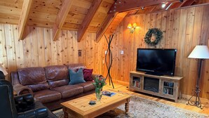 A cozy living room with a brown leather sofa, wooden coffee table, and a flat-screen TV on a wooden stand.