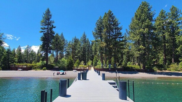 A wooden pier extending into a clear lake, surrounded by dense forest.