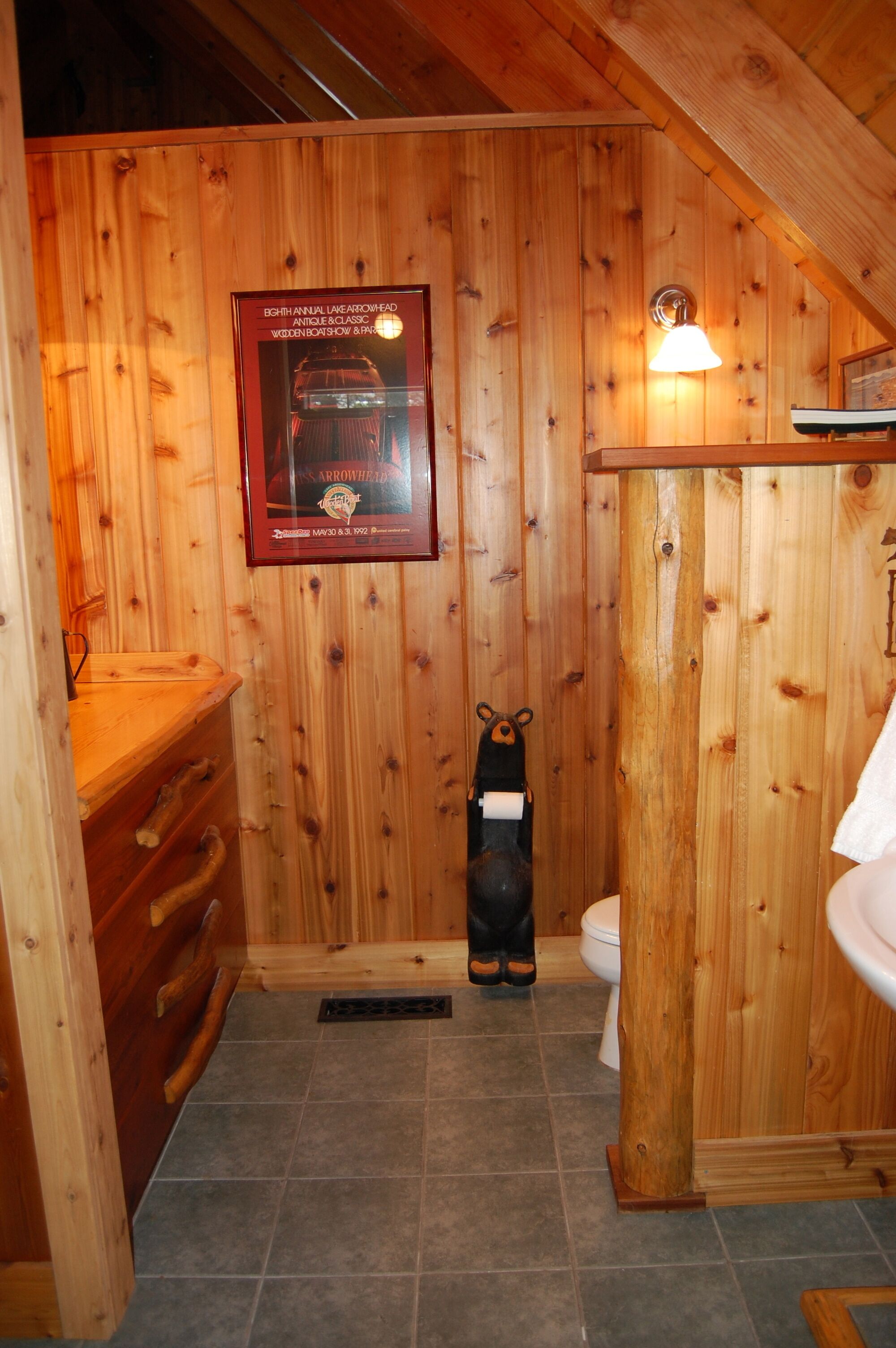 Un baño de cabaña de madera con un certificado enmarcado en la pared, un perchero con forma de oso y un tocador de madera.