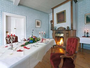 A dining room with a fireplace, a table set for a meal, and a red upholstered chair.