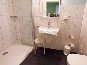 A bathroom with a shower, sink, toilet, and a small stool.