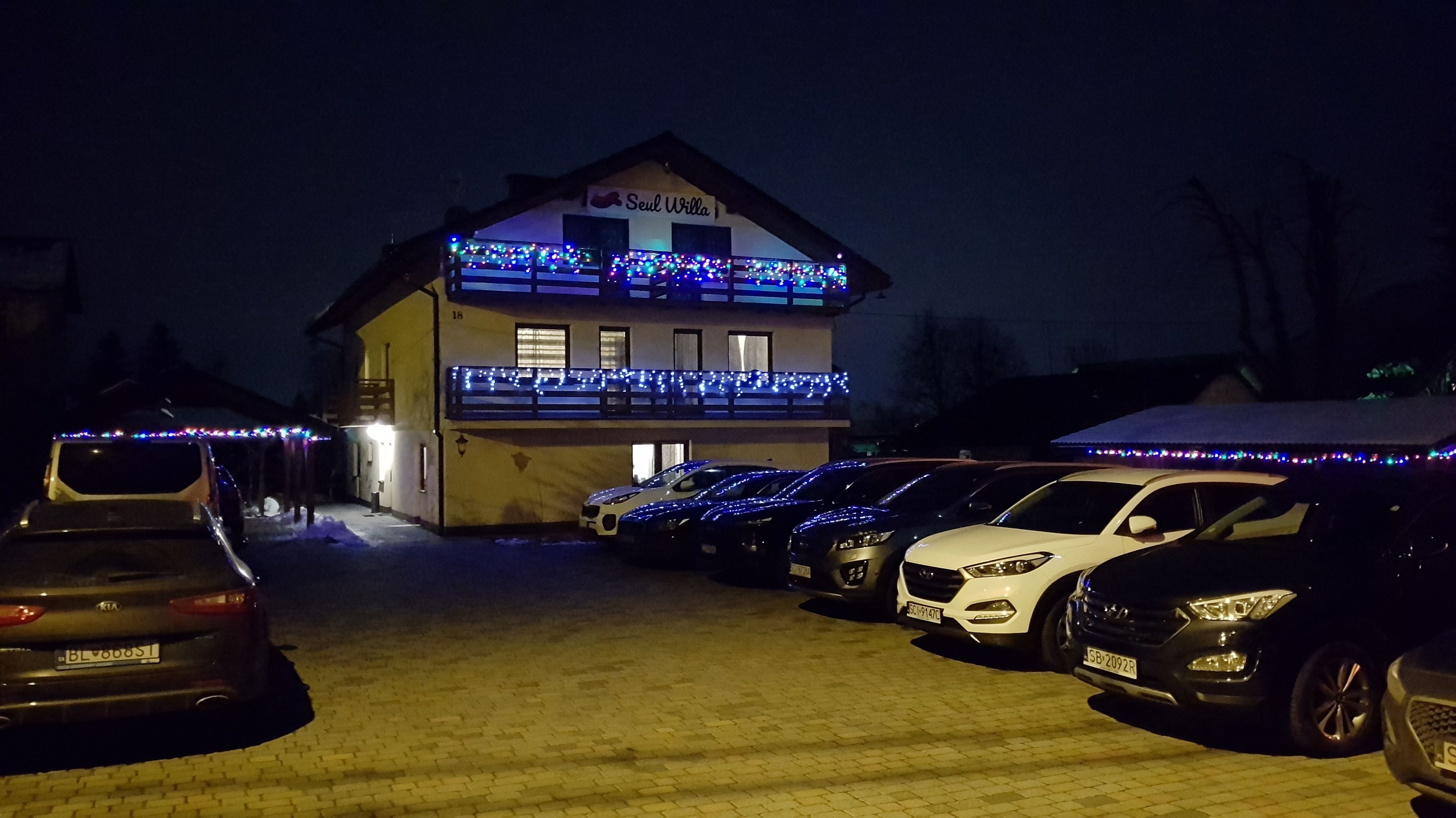 A building with a sign reading "Seul Vila" and a parking area with several cars.