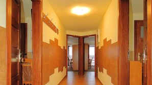 A hallway with wooden doors and tiled flooring, leading to a dining area with a table and chairs.