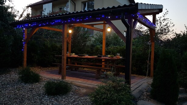 A wooden pergola with blue string lights, a picnic table, and a hanging light fixture.